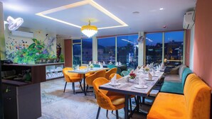 A restaurant with a long dining table, orange chairs, and a green sofa. - Hotel Lords Valley Rishikesh (Rishikesh)