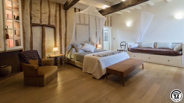 Une chambre à coucher comprenant un lit, des tables de chevet, une chaise, un banc et une fenêtre avec des étagères à livres.