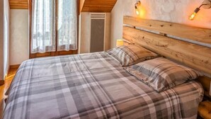 Ein Schlafzimmer mit Holzboden, einem Bett mit kariertem Überwurf und zwei Wandleuchten.
