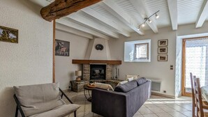 Ein gemütliches Wohnzimmer mit Kamin, einer Couch, einem Sessel und einem Holzbalken an der Decke.