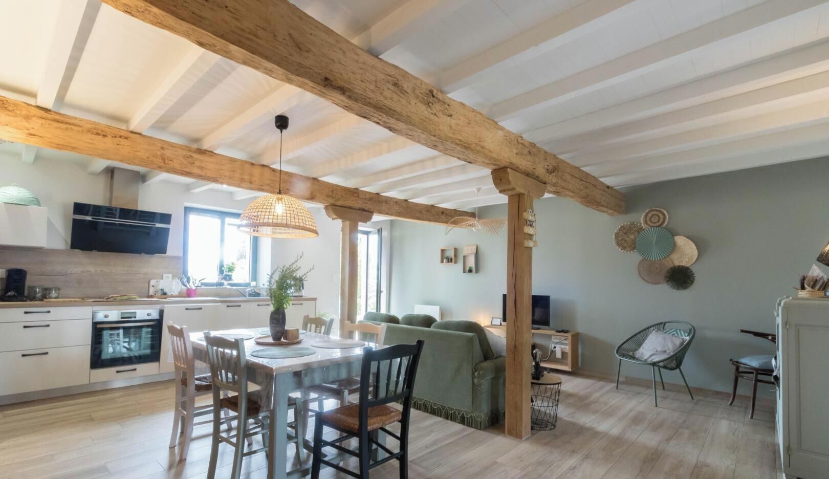 A spacious living area with a wooden ceiling, a dining table with chairs, a sofa, and a television.