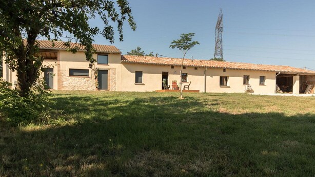 A two-story building with a tiled roof, a grassy yard, and a power line tower in the background. - Gîte La Selve d'Autan - Caraman (Caraman)
