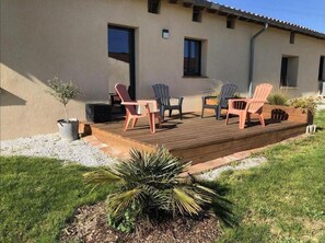 Ein Gebäude mit einer Holzterrasse, Sitzgelegenheiten im Freien und einem kleinen Garten.