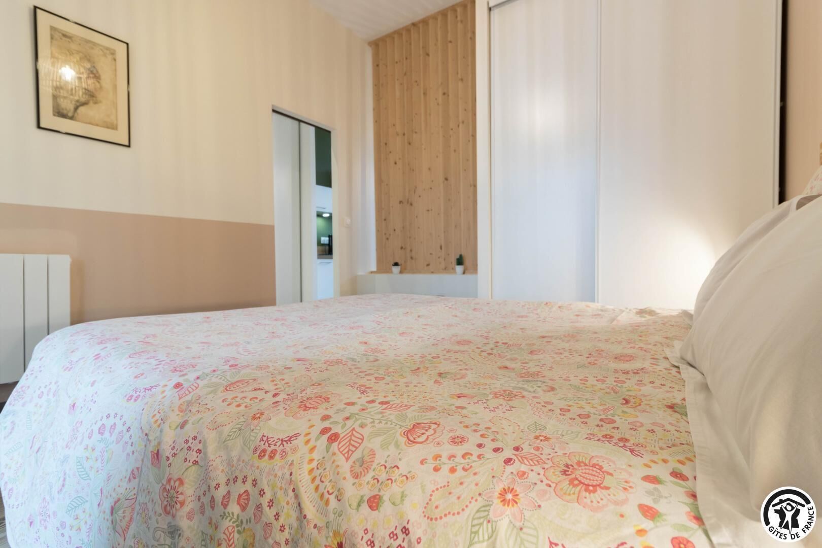 Une chambre à coucher avec une couvre-lit à motifs floraux, une tête de lit en bois et un tableau encadré accroché au mur.