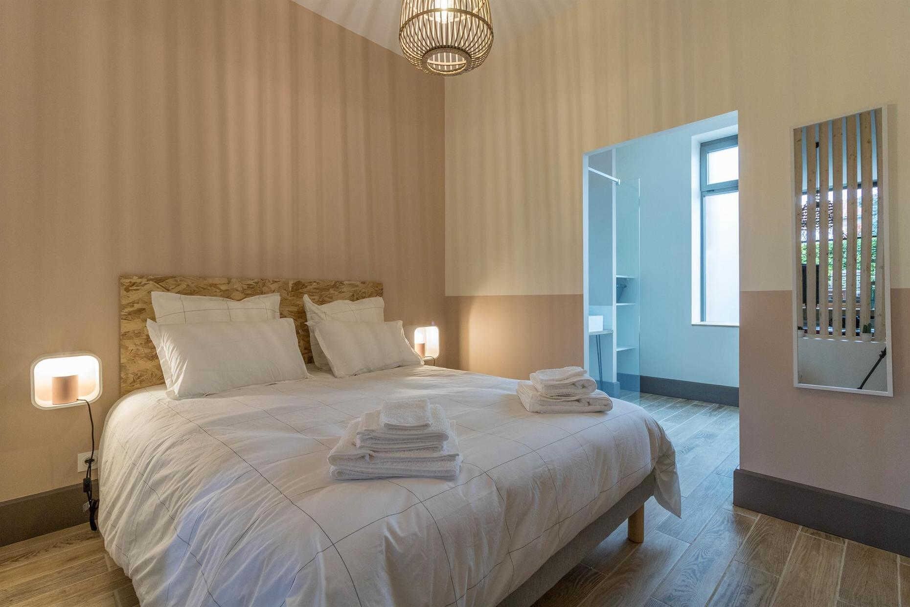 A hotel room with a large bed, two bedside lamps, a chandelier, and a view of a balcony.