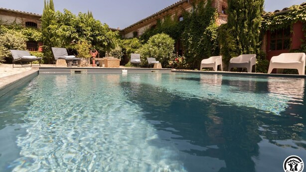 A swimming pool with lounge chairs and a brick building in the background.