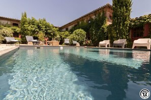 A swimming pool with lounge chairs and a brick building in the background.