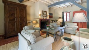 A spacious living room with a fireplace, a large wooden cabinet, and several white sofas.