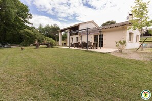 A house with a covered patio, a lawn, and a garden with potted plants. - Villa Les Paradoux - Pin-Balma (Pin-Balma)