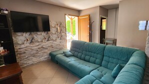 Ein Wohnzimmer mit einem türkisfarbenen Sofa, einem Flachbildfernseher, einer Steinwand und einer Holztür, die nach draußen führt.