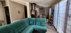 Una sala de estar con un sofá modular, un pilar de piedra, un comedor con mesa y sillas, y una zona de cocina con un frutero.
