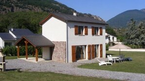 Ein zweistöckiges Haus mit Steinunterbau, geneigtem Dach und einer überdachten Terrassenfläche.