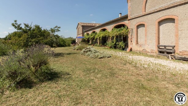 A building with a brick facade, arched windows, and a garden area with lavender plants.