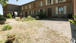 A building with a courtyard, featuring a brick facade, arched windows, and a gravel ground.