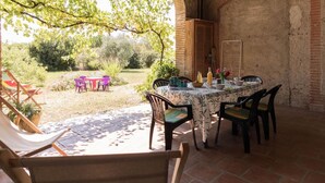 An outdoor patio with a round table and chairs, surrounded by a brick wall and covered by a wooden arch.