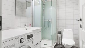 A modern bathroom with a glass-enclosed shower, a washing machine, and a toilet.