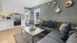 A modern living room with a grey sofa, a coffee table, and a kitchen area with white cabinets and a microwave.