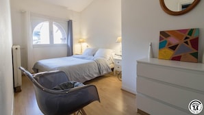 A bedroom with a bed, bedside tables, a chair, a dresser, a window with curtains, and a painting.