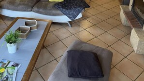 A modern living room with a sofa, a coffee table, and a fireplace. There is a kitchen area in the background with a dining table and chairs. - Gîte des Cyprès - Bérat - Gîte (Bérat)