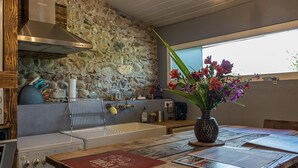 Una cocina con pared de piedra, estufa y un florero con flores sobre la mesa.