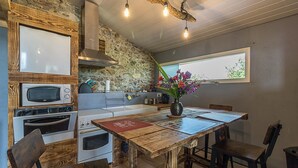 Una cocina con pared de piedra, hornos empotrados y zona de comedor con mesa y sillas de madera.