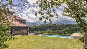Una casa de fachada de piedra, techo de tejas y piscina en el patio trasero.