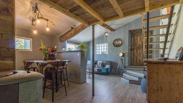 Un interior rústico con una mesa de comedor de madera, taburetes de bar, un sofá y una escalera.