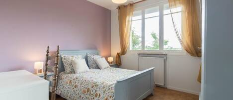 A bedroom with a bed, bedside lamps, a window with curtains, and a radiator.