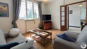 Una sala de estar con sofá, mesa de centro, televisor y una puerta que da a otra habitación.
