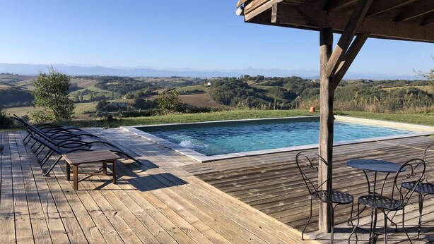 A wooden deck with a pool, outdoor seating, and a view of rolling hills.