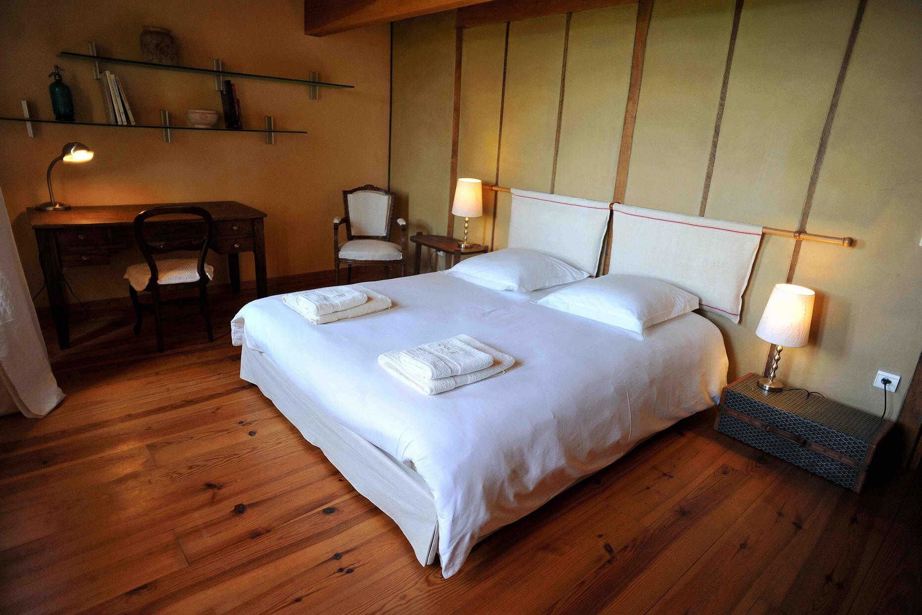 Une chambre bien rangée, avec un grand lit, des lampes de chevet, un bureau et une chaise.