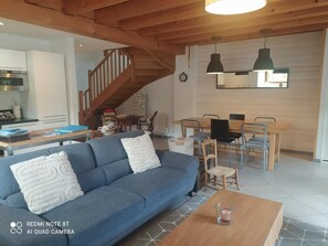 A modern living room with a blue sofa, wooden dining table, and a staircase.