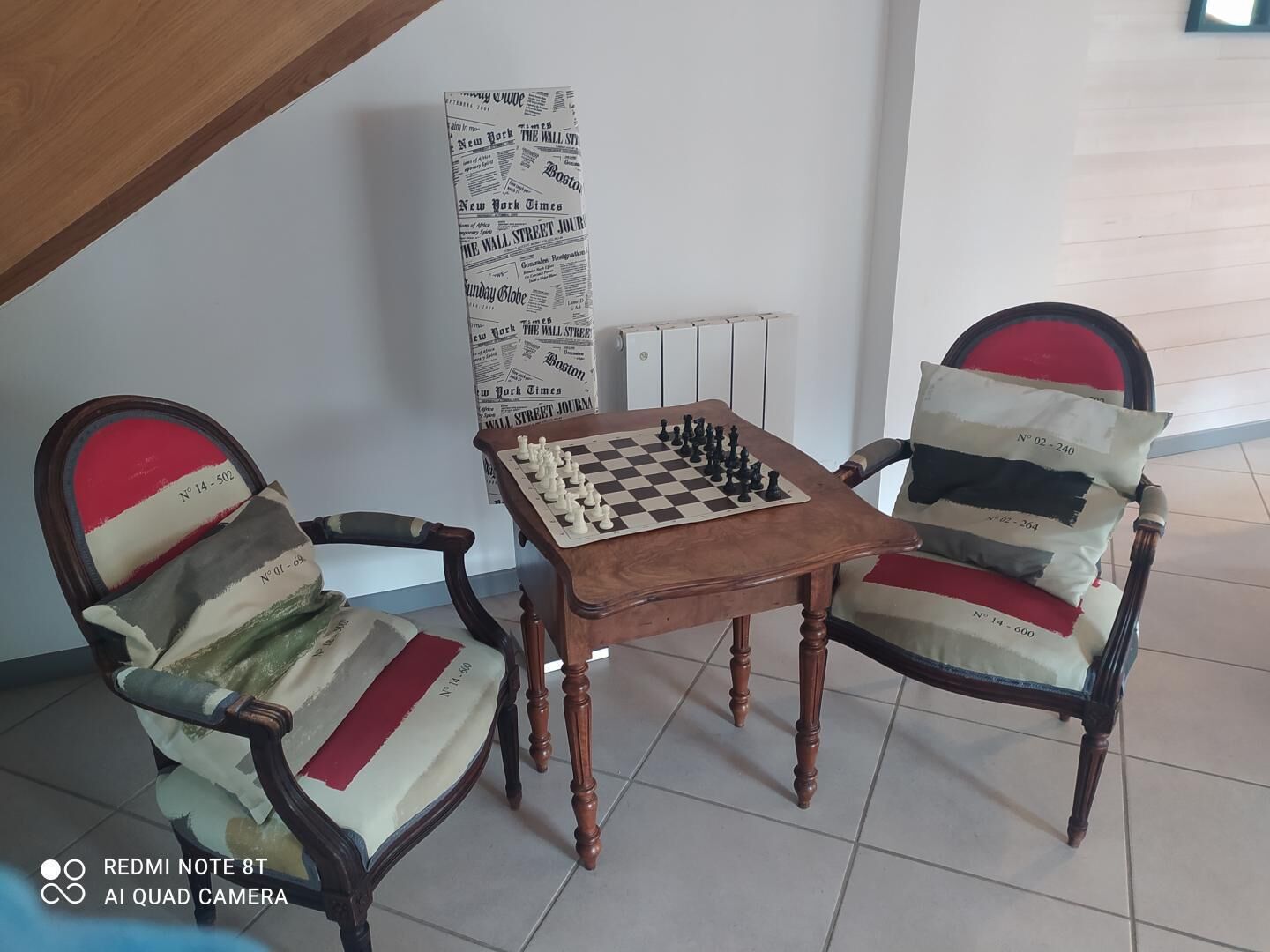 Un tablero de ajedrez sobre una pequeña mesa, con dos sillas tapizadas.