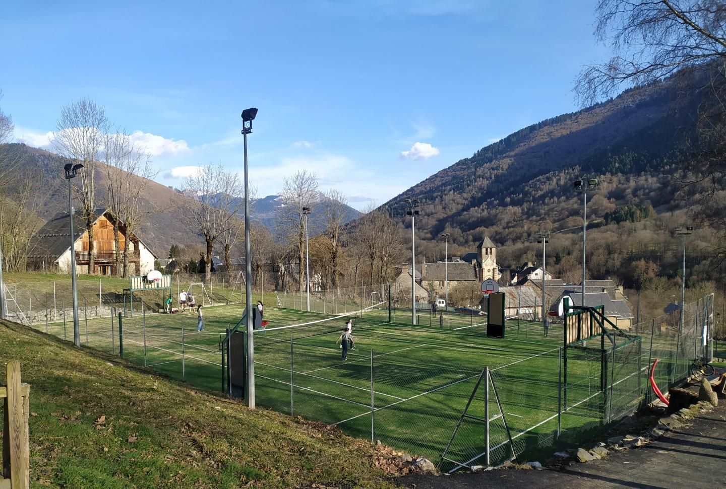 A tennis court with a net, surrounded by a fence, and a building in the background.