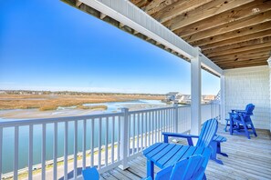 A wooden deck with blue Adirondack chairs overlooking a river and marshland.