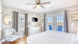 A bedroom with a large bed, a ceiling fan, a dresser, a chair, and a TV. - Cayman Villas Unit D-1 (North Myrtle Beach)
