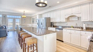 A spacious kitchen with white cabinetry, a granite countertop, and a central island with bar stools. - Cayman Villas Unit D-1 (North Myrtle Beach)