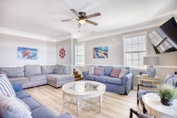 A living room with a sectional sofa, a glass coffee table, and a ceiling fan.