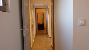 A narrow hallway with a tiled floor, leading to a room with a door and a light switch on the wall.