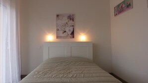 A bedroom with a bed, a headboard, a wall-mounted picture, and a window with curtains.