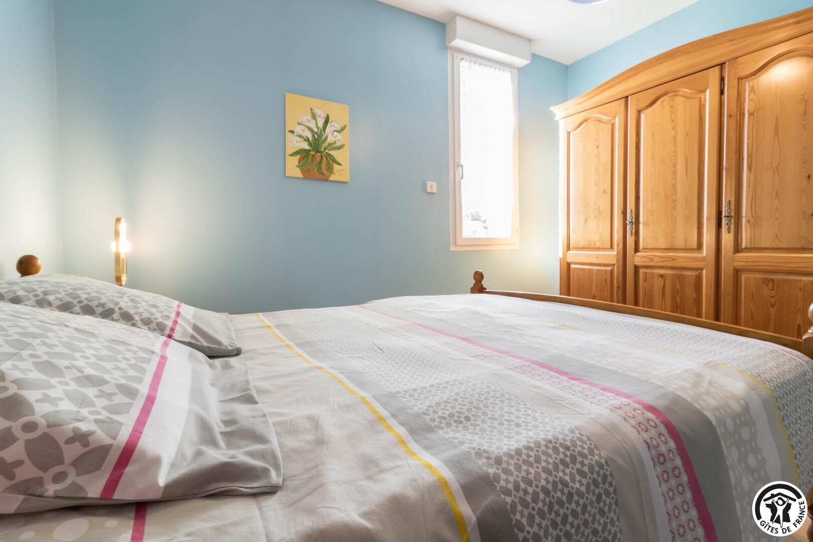Een slaapkamer met een bed, een houten garderobe, een raam en een schilderij aan de muur.