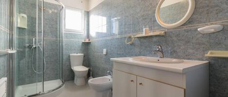 A bathroom with a glass-enclosed shower, a toilet, a bidet, and a sink with a mirror above it.