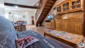 Un salon comprenant un canapé, une table basse avec des magazines, un meuble en bois, un téléviseur et un escalier.