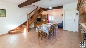 Une cuisine spacieuse avec un escalier en bois, un coin repas avec une table et des chaises, et un four en briques.
