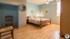 Une chambre à coucher avec un lit en bois, une chaise, un miroir rond et une fenêtre avec des rideaux.