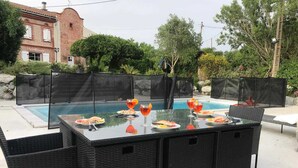 Un área de comedor al aire libre con piscina, rodeada por una cerca, y un edificio al fondo.