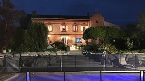 Un edificio de ladrillo con una escalera que conduce a la entrada, rodeado de follaje y un muro de piedra.