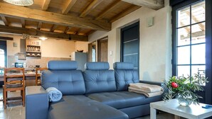 Ein modernes Wohnzimmer mit einem Ecksofa, einem Essbereich mit Holzsesseln und einer Küche im Hintergrund.