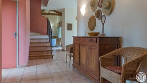 Un escalier menant à un deuxième étage, une chaise en osier, un meuble en bois et un mur orné de chapeaux tressés.