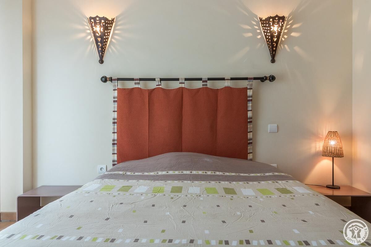 A neatly made bed with a striped headboard, two wall sconces, and a bedside lamp.